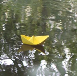 Gevouwen bootje van geel papier dat voortdrijft op rustig water
